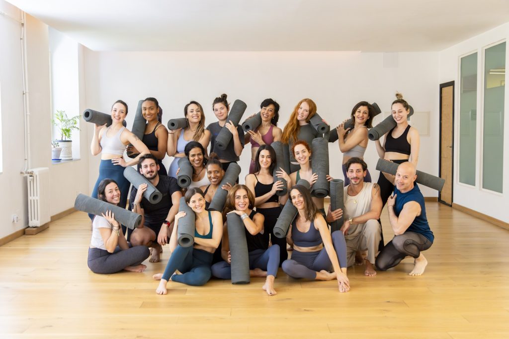 Diverse group of yoga practitioners holding rolled mats, smiling in a bright studio after a successful workout