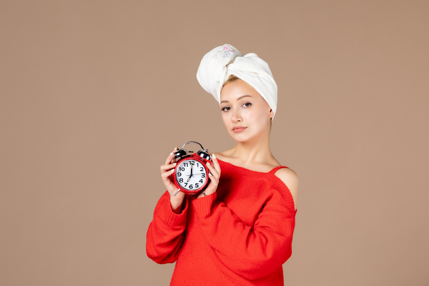 front view young female holding clocks with towel on her head on pink background woman shower spa massaging mask skincare cream hair