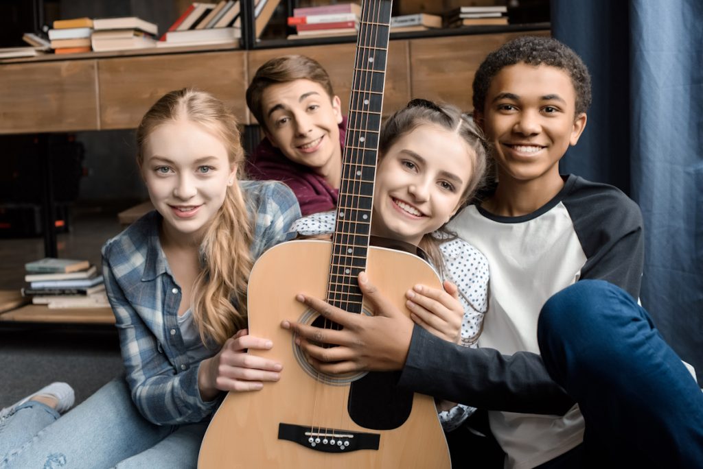 front view of happy teenagers holding guitar at home, teenagers playing guitar concept