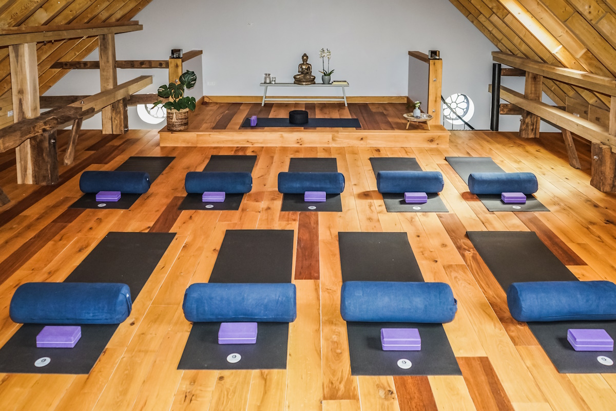 An inviting yoga studio with a calming atmosphere, featuring neatly arranged yoga mats, bolsters, and blocks on a wooden floor, with soft natural lighting and minimalistic decor.