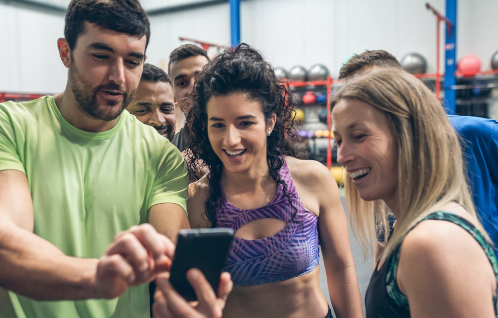 Group of athletes laughing looking at the mobile of a gym mate