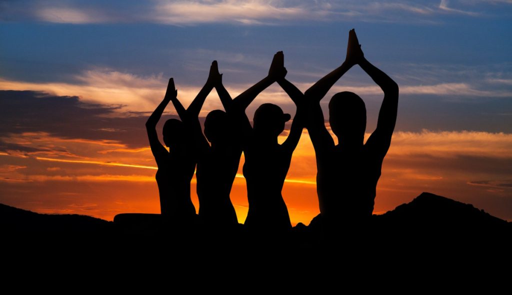 Silhouette of people practicing yoga against sun. Sunset meditation concept