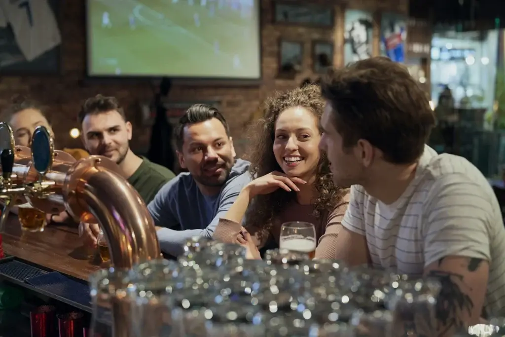 A group of friends enjoying drinks at a bar, with a TV in the background showing a sports game.